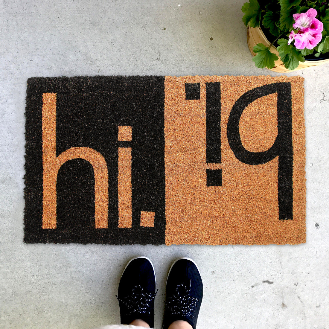 A black and brown coir doormat with the text 'hi bi' printed prominently, placed on a doorstep with a pair of shoes at the bottom of the image.