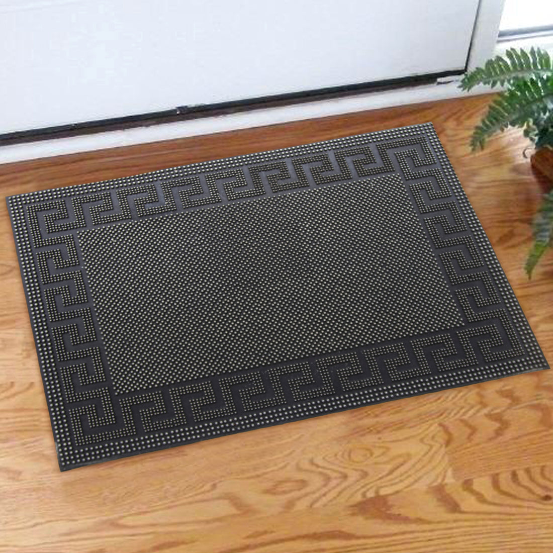 A black rubber pin mat with a Greek design border placed on a wooden floor, near the entrance of a home.