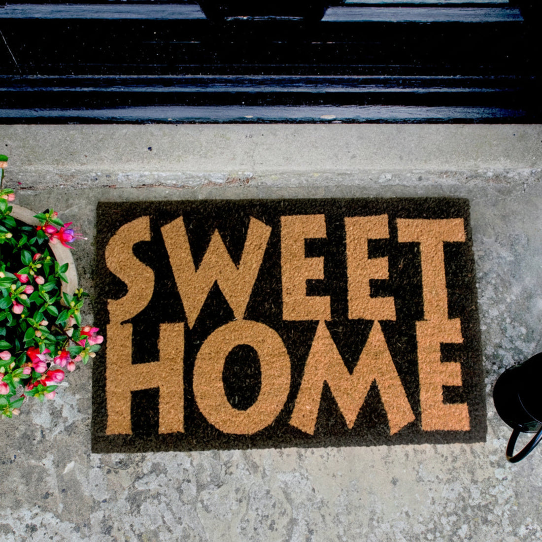Rectangular natural coir door mat with the text 'SWEET HOME' printed in brown, placed on a doorstep.