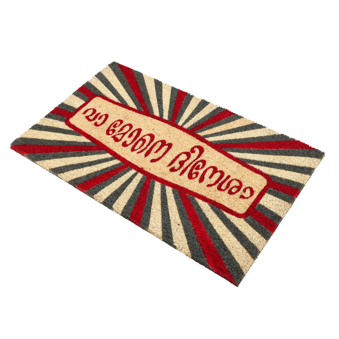 A colourful doormat with a funny welcome message 'Va Mone Dinesha ' in Malayalam, featuring a red and yellow circular design with a black ring in the centre, and a black and white striped pattern towards the bottom.