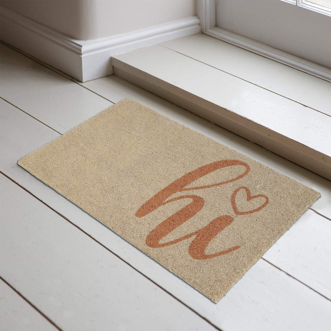 A beige natural coir entrance doormat with a 'Hi' printed design in a heart shape, placed on a light wooden floor.