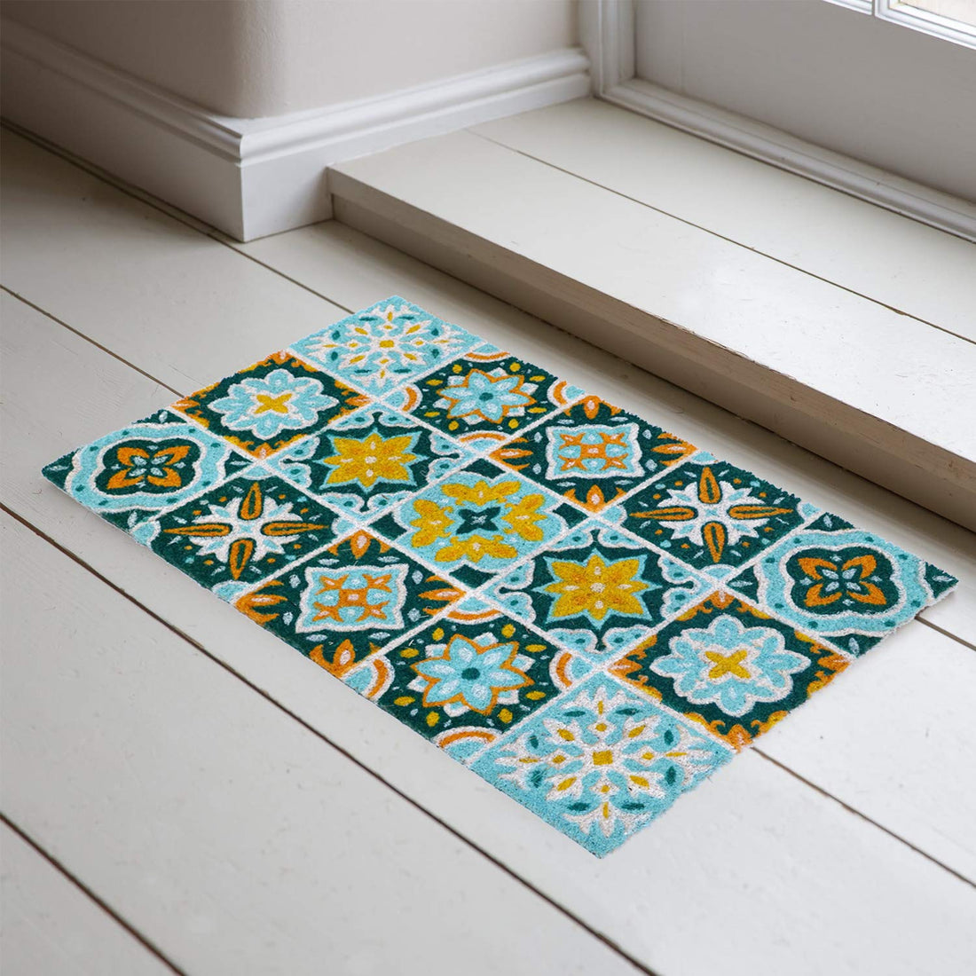 A rectangular natural coir door mat with a colourful floral mosaic tile pattern placed on a white floor.