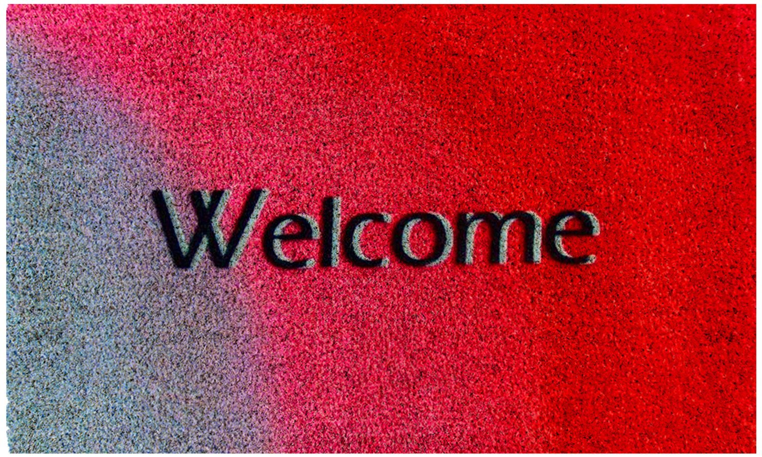 A rectangular natural coir door mat with the word 'Welcome' printed in grey on a red background.