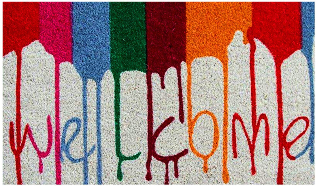 A colourful door mat with a welcoming message printed in a watercolour style on a white background.