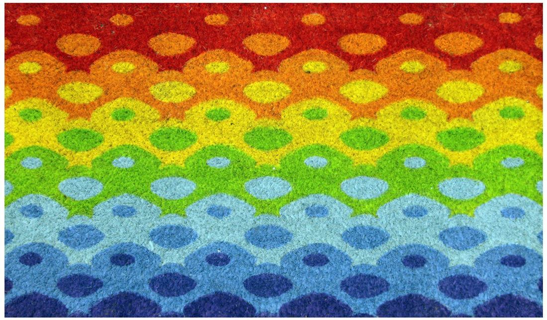 A rectangular natural coir floor mat with a colourful geometric pattern featuring a Holi theme.