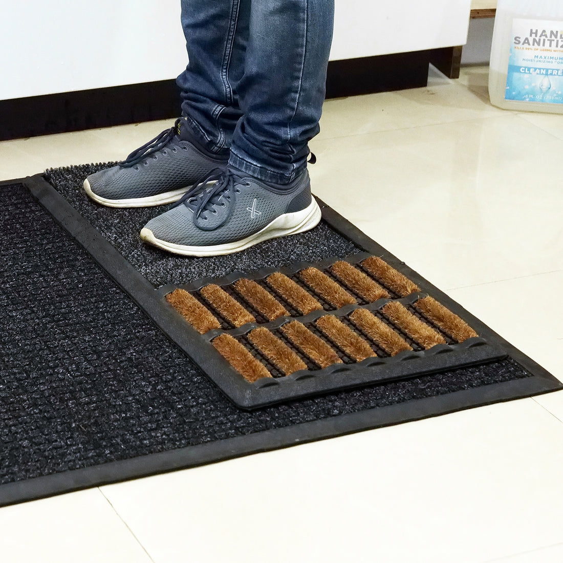 A person stepping on a black sanitizing mat with a polypropylene insert at an office entrance