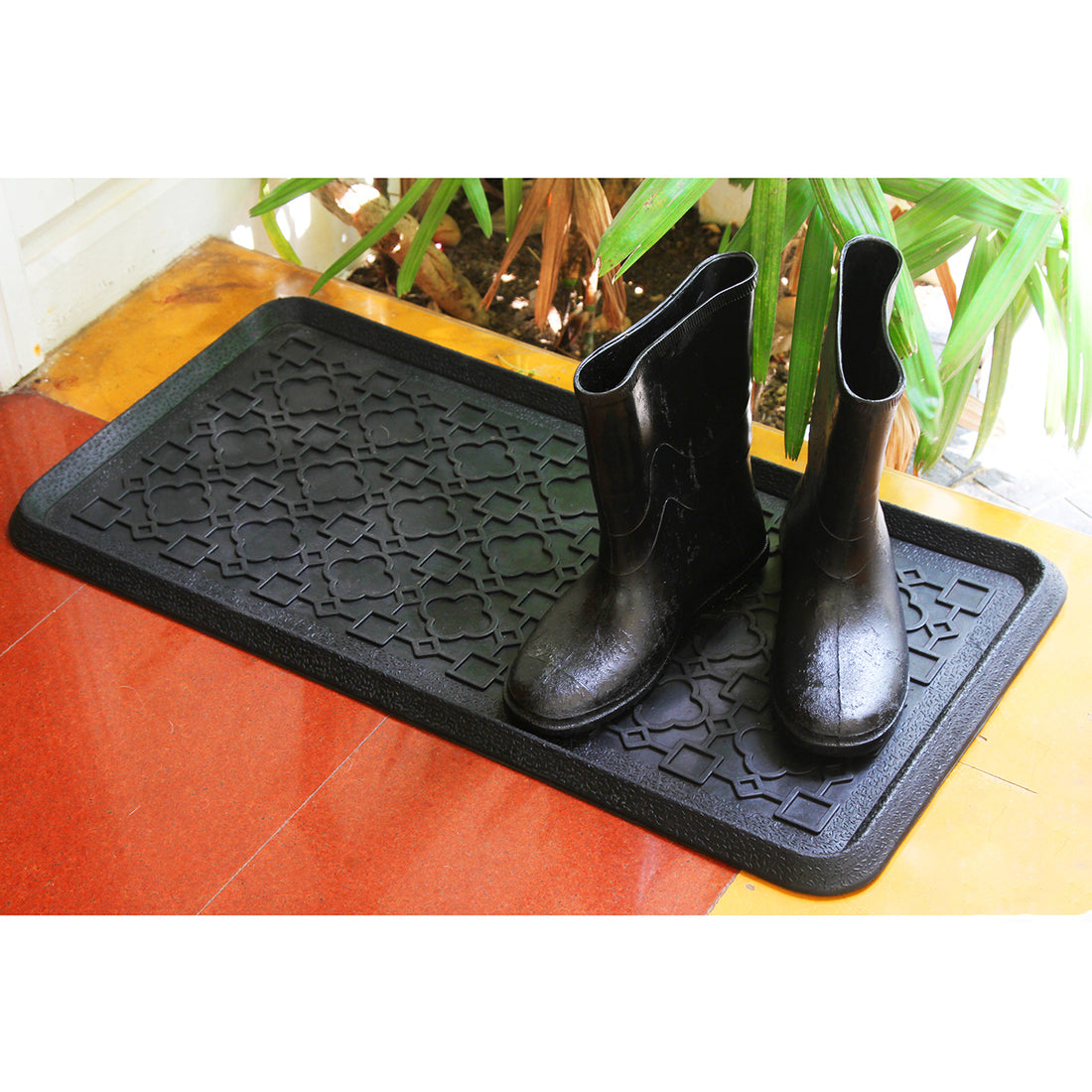 Black rubber boot tray with a geometric pattern, placed on the floor, with boots placed on top of it.