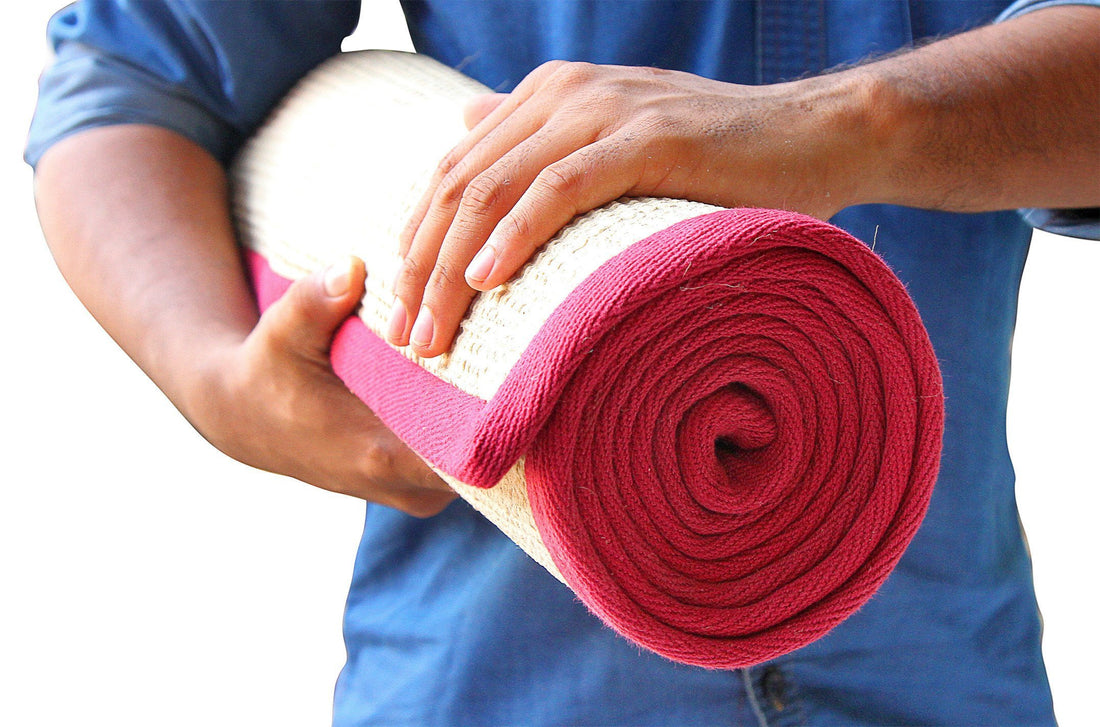 
                      
                        A rolled-up yoga mat with a maroon cotton border and natural jute colour visible in the centre.
                      
                    