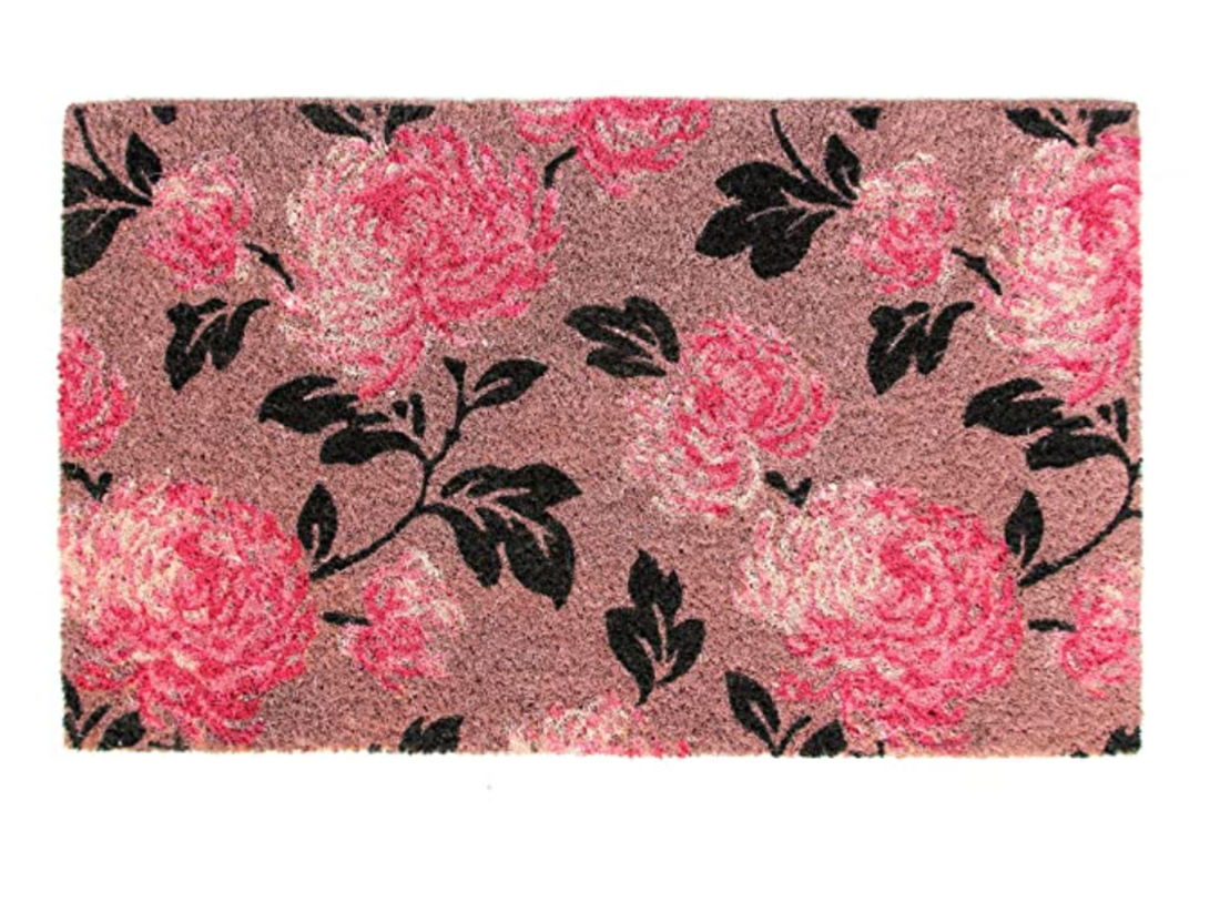 A rectangular coir doormat with a floral pattern in pink and black colors.