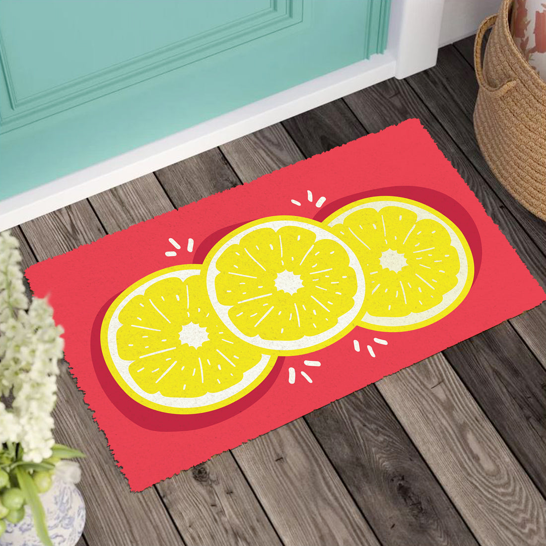 A red floor mat with a colourful lemon print design, placed on a wooden floor, with a blue door in the background and a wicker basket to the side.