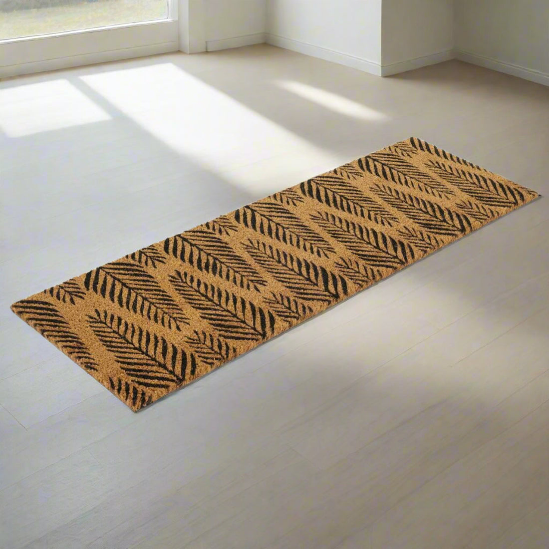 
                      
                        A rectangular natural coir entrance door mat with a pine leaf printed design, placed on a light-colored floor.
                      
                    