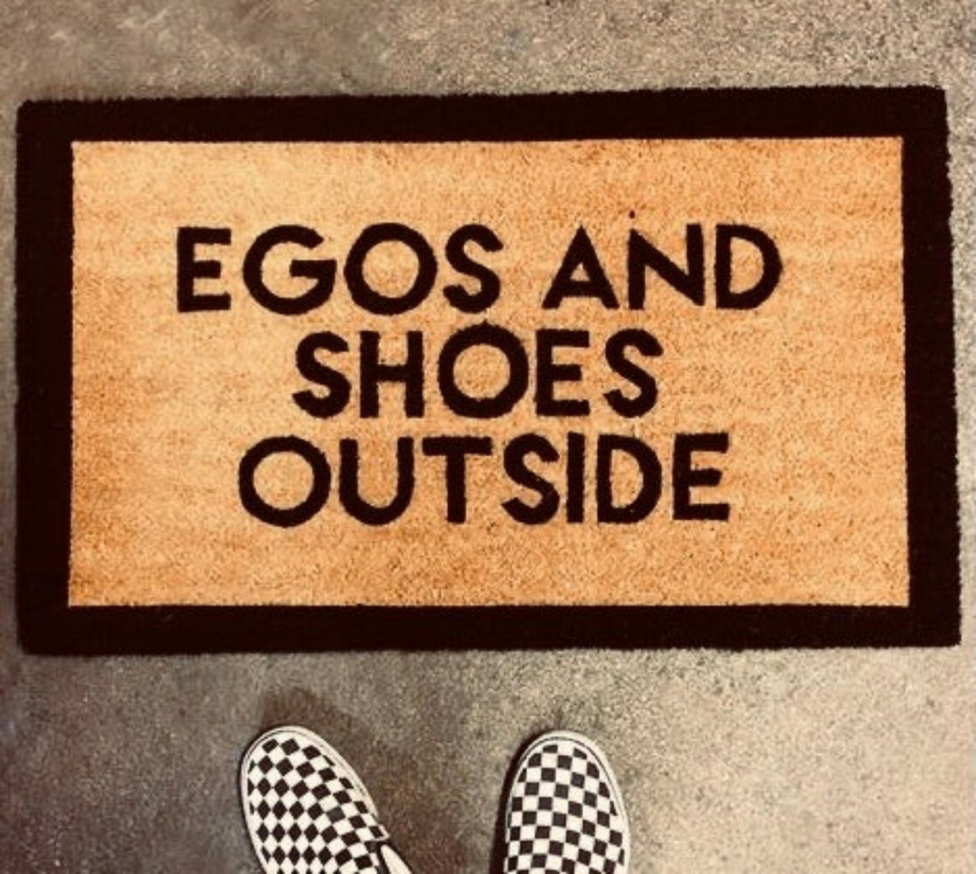 Doormat with 'EGOS AND SHOES OUTSIDE' text on a textured surface.