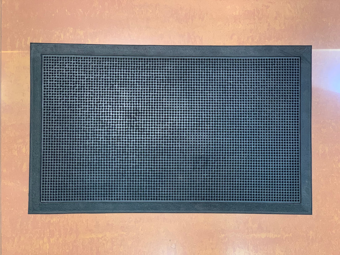 A black rectangular rubber mat with a textured surface and small rubber studs designed for trapping dirt and sanitising shoes.