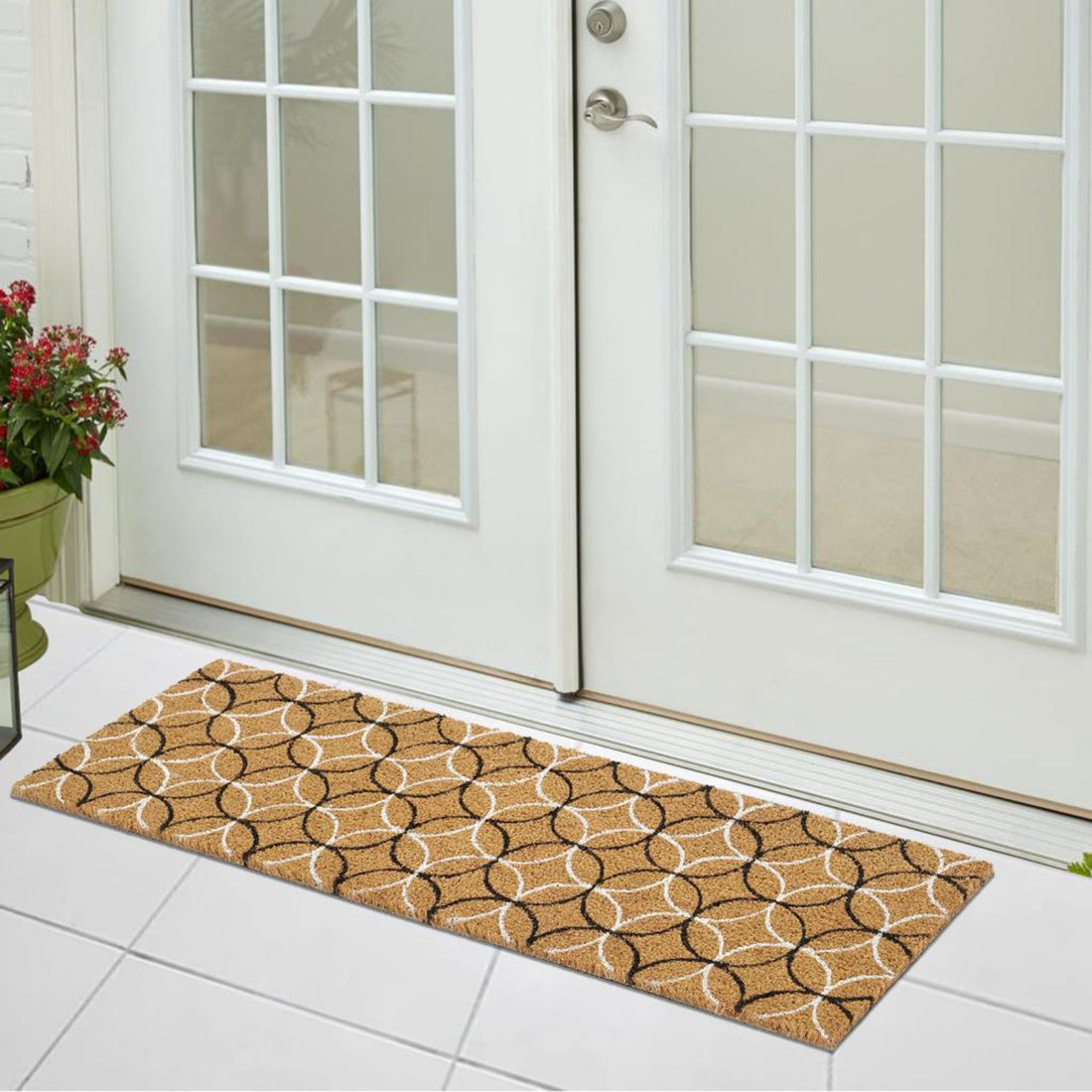 Circle-patterned doormat in front of a glass door with flowers on the left.