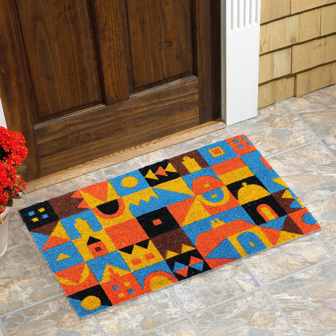 
                      
                        A rectangular natural coir door mat with a colourful mosaic pattern design is placed on a tiled floor in front of a wooden door.
                      
                    