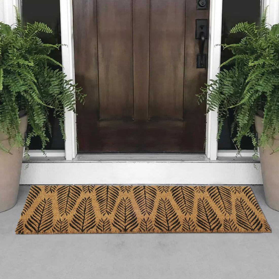 Coir doormat with leaf pattern in front of a door with plants on either side.