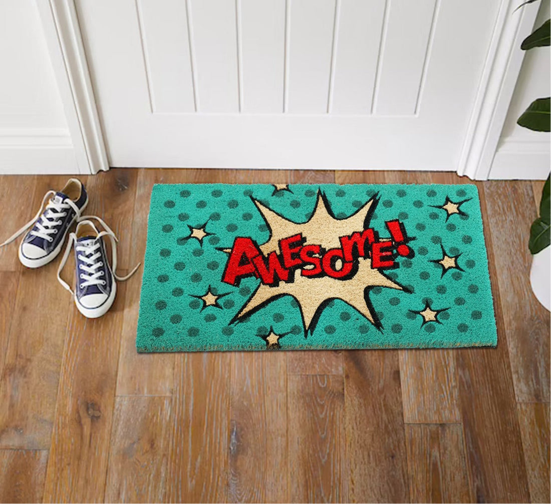 
                      
                        A rectangular natural coir door mat with a colorful pop art design featuring the word 'AWESOME' in the center, placed on a wooden floor next to a pair of sneakers.
                      
                    