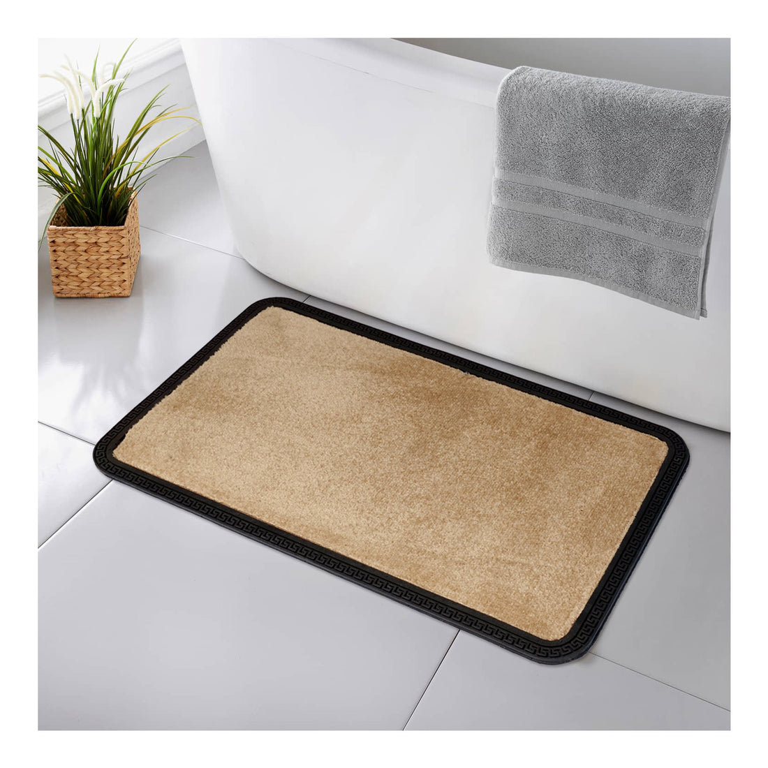 A beige rectangular bath mat with a black border, placed on a tiled bathroom floor, near a wicker basket with a towel and a potted plant.