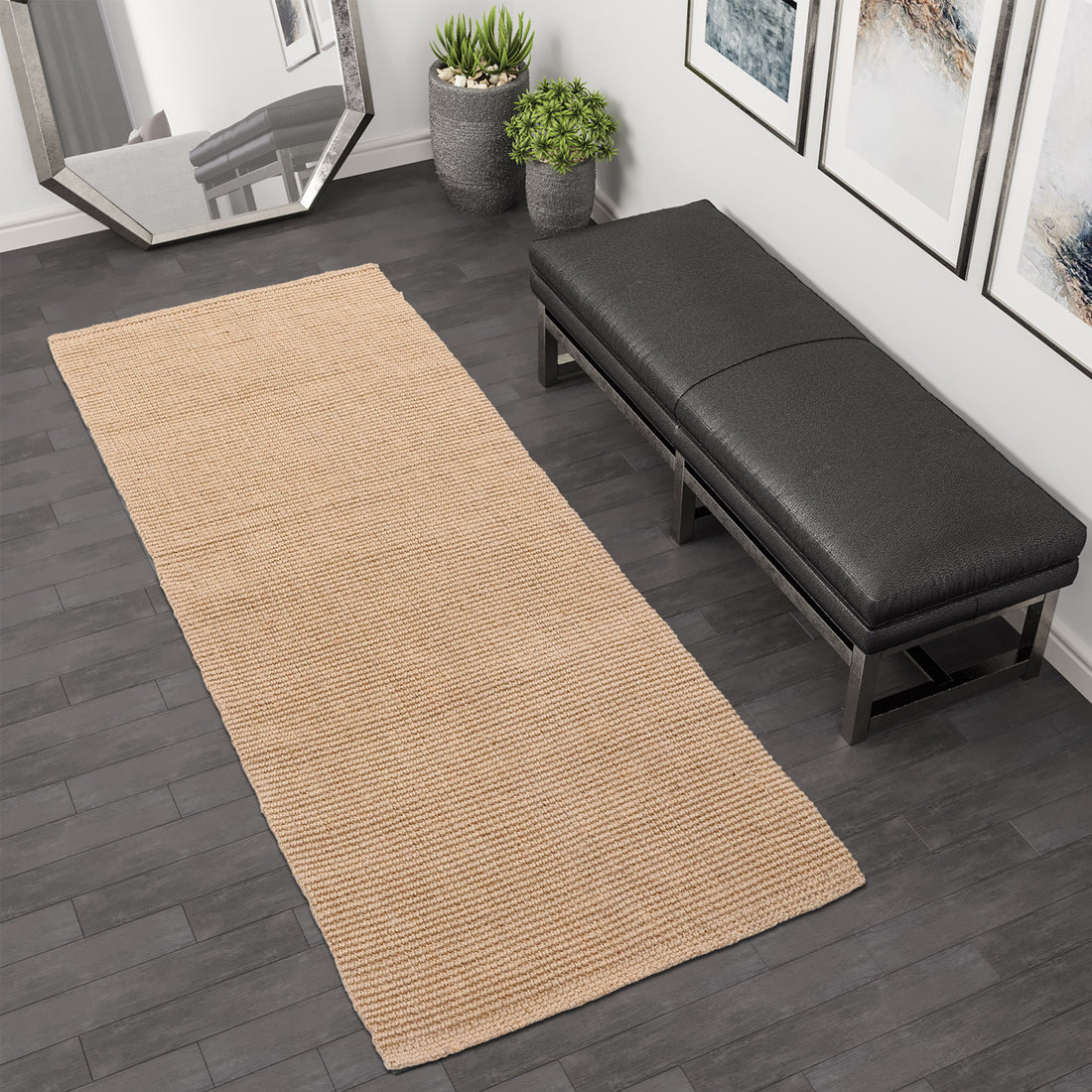 A flatweave construction jute runner rug in a natural brown colour, placed on a tiled floor next to a black bench, with a decorative mirror and plant in the background.