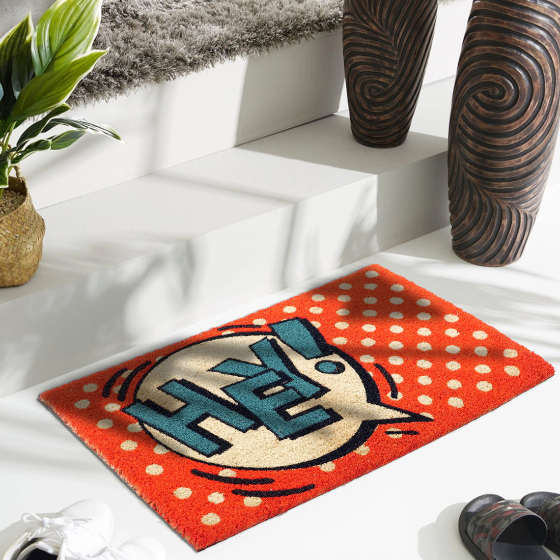 A rectangular natural coir door mat with a pop art fun design, featuring a blue and red color scheme and the text 'HEY' printed on it, placed on a white step in a home environment.
