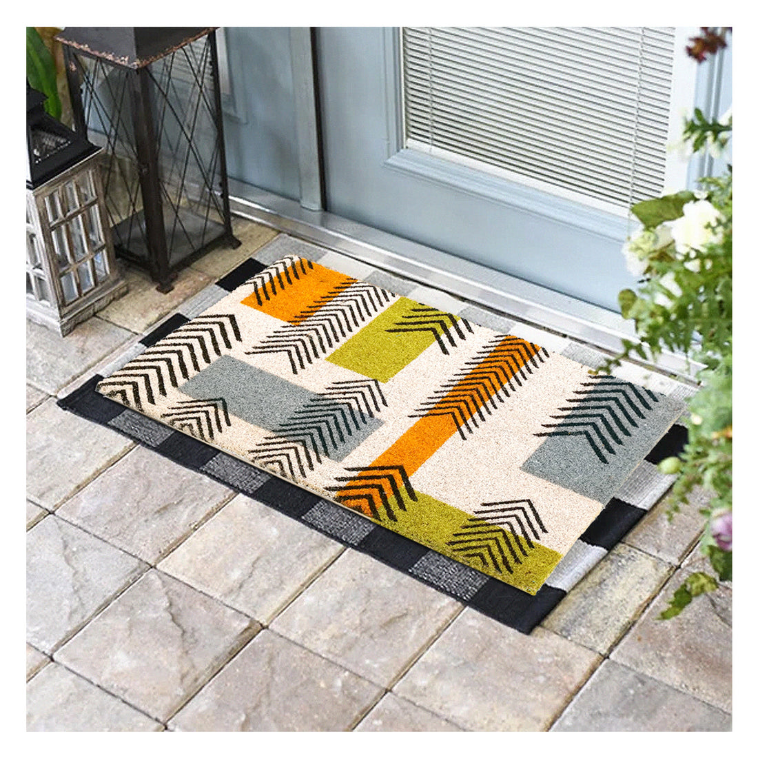 A multicoloured geometric-patterned door mat made of natural coir, featuring arrows in shades of green and orange, placed on a tiled floor by a door.