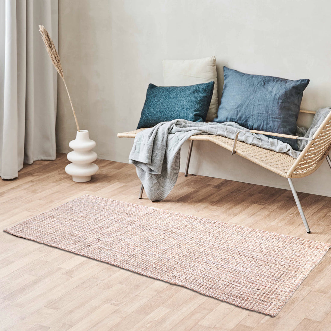 A rectangular jute runner rug in pink and white, placed on a wooden floor beside a wicker sofa with pillows and a decorative vase.
