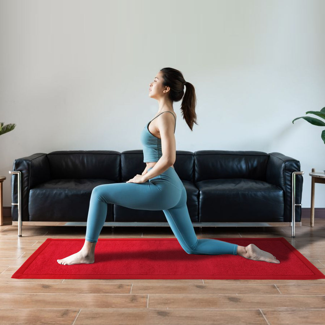 A person practicing yoga on a red yoga mat in a living room with a black sofa in the background.