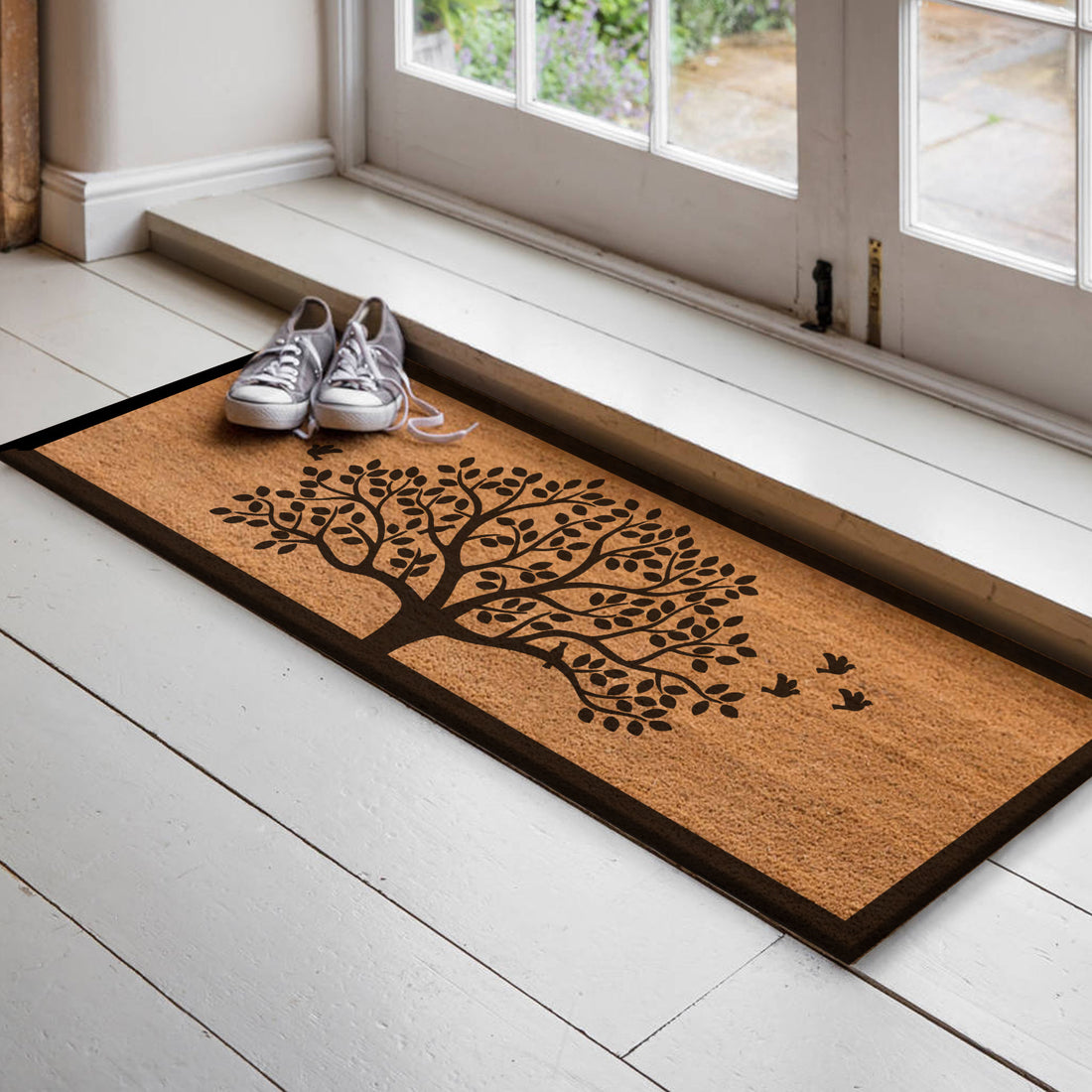 A natural coir doormat with a Tree of Life and birds print placed on a white floor, leading up to a set of French doors.