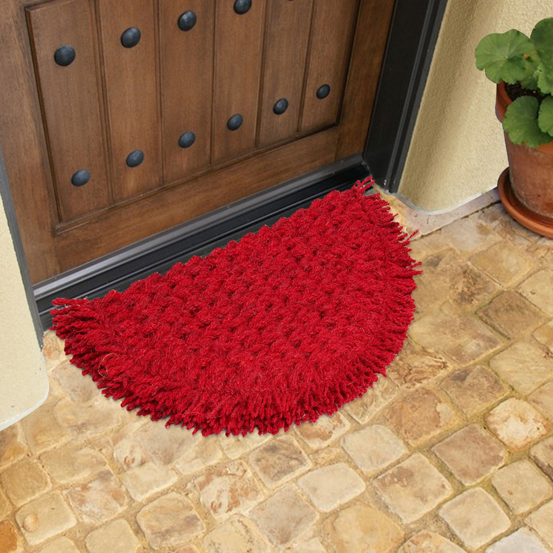 A red semi-circle coir rope mat with fringes placed on a tiled floor in front of a wooden door, featuring a sunrise design.