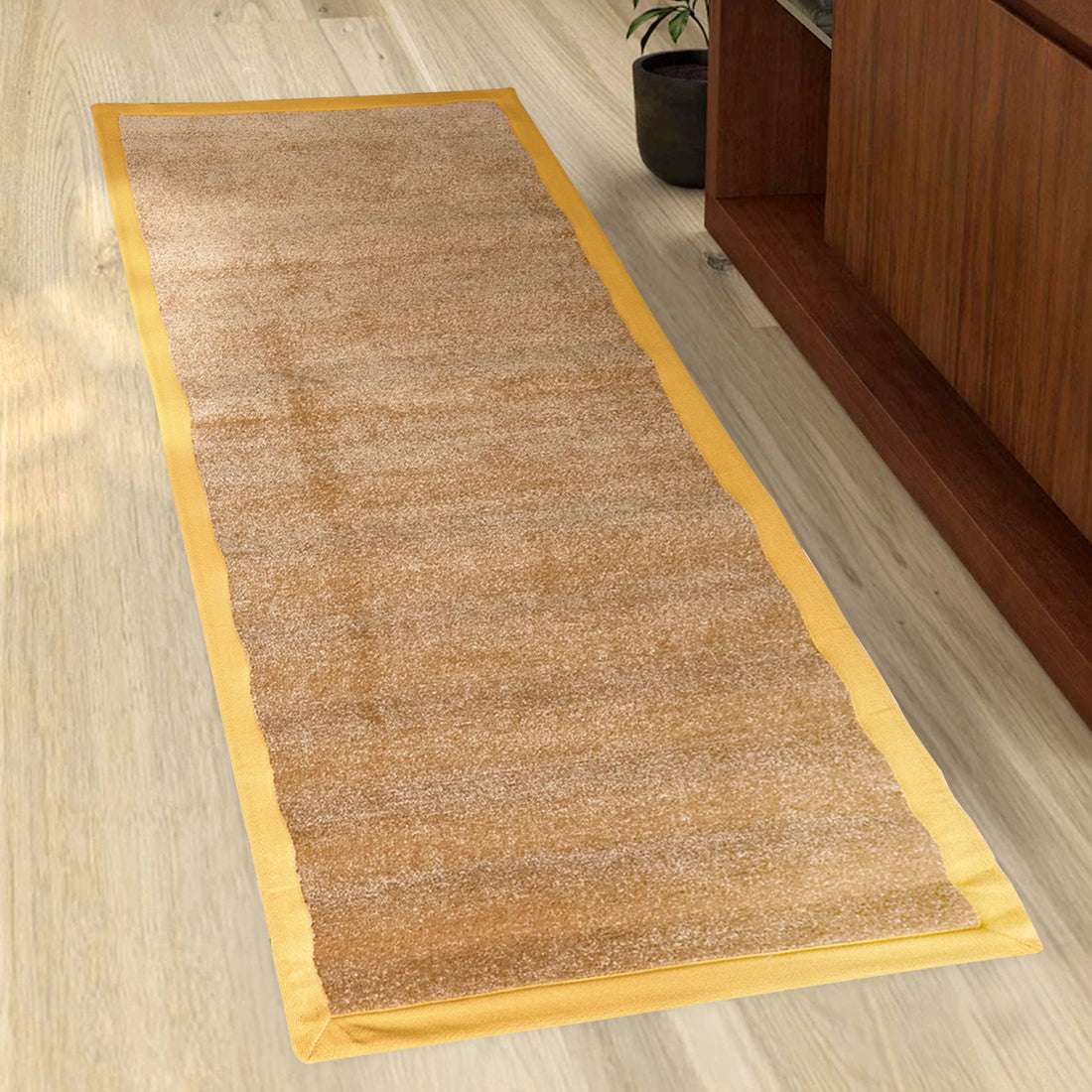 A beige yoga mat with a yellow border, placed on a wooden floor with a cabinet in the background.