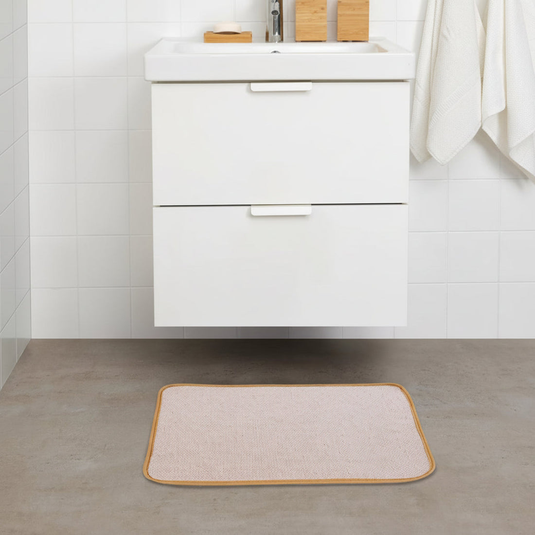 A cream-colored rectangular mat with a solid pattern is placed on a tiled floor in front of a white bathroom cabinet.