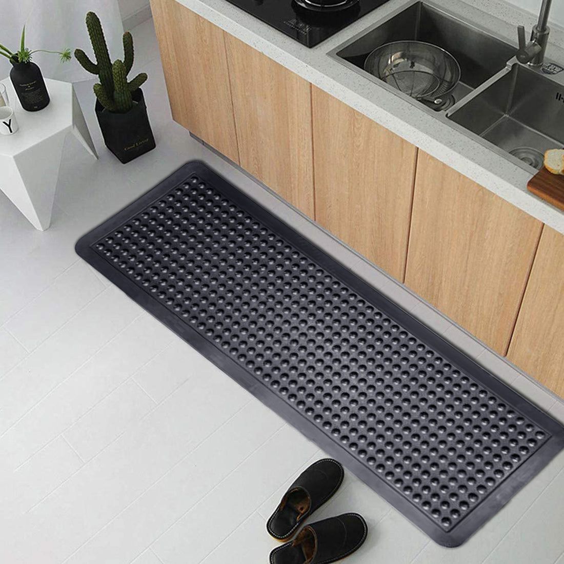 A black Onlymat Anti Fatigue Bubble Surface Rubber Mat placed on a kitchen floor, extending from the doorway to the inside, with a pattern of bubbles on its surface.