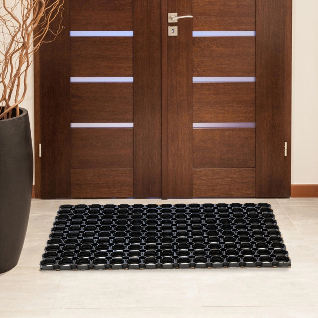 A black, rubber flexible hollow mat with a hexagonal pattern, placed on a floor in front of a wooden door entrance.