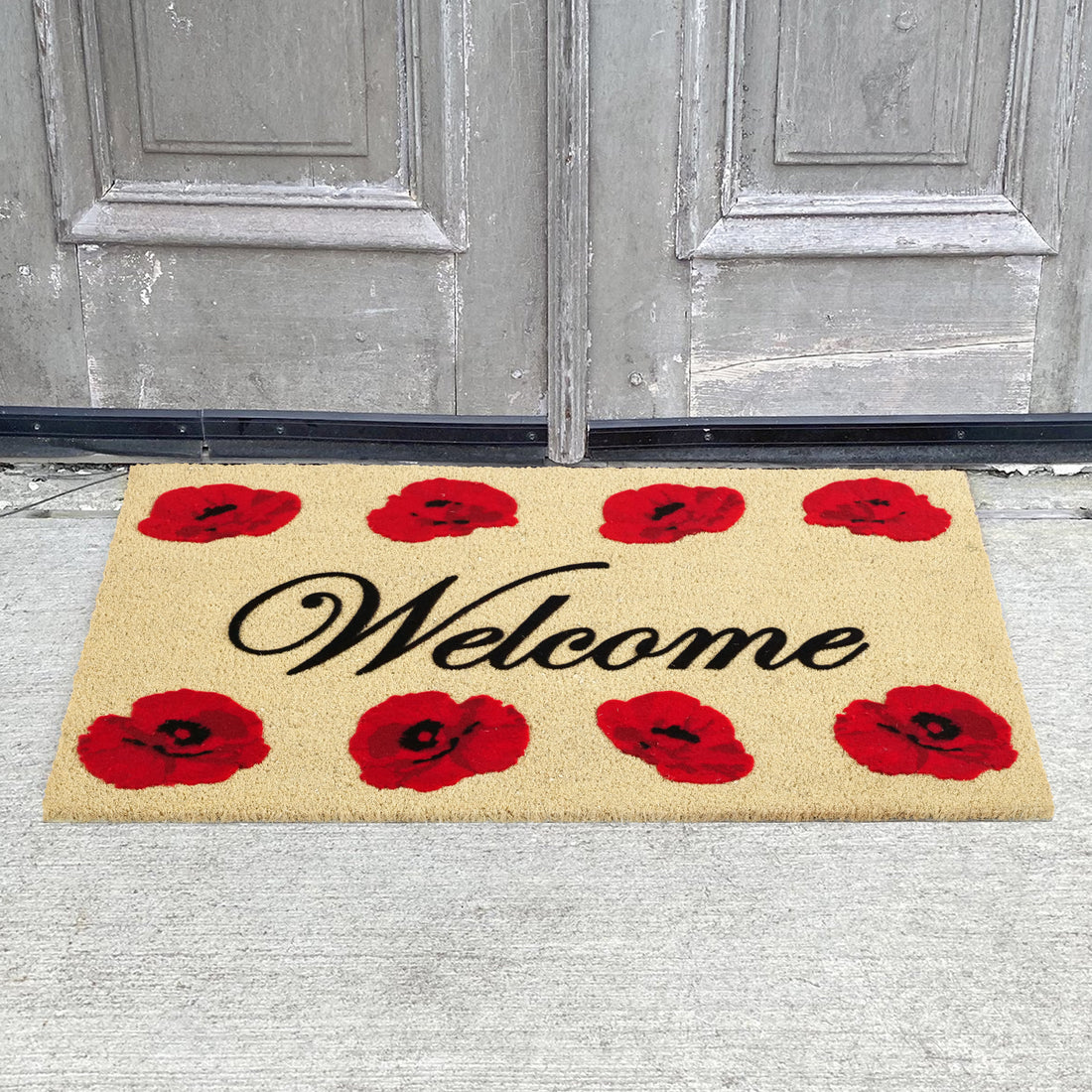 A rectangular coir door mat with a bleached background and red poppy flower prints, featuring the word 'WELCOME' in bold.