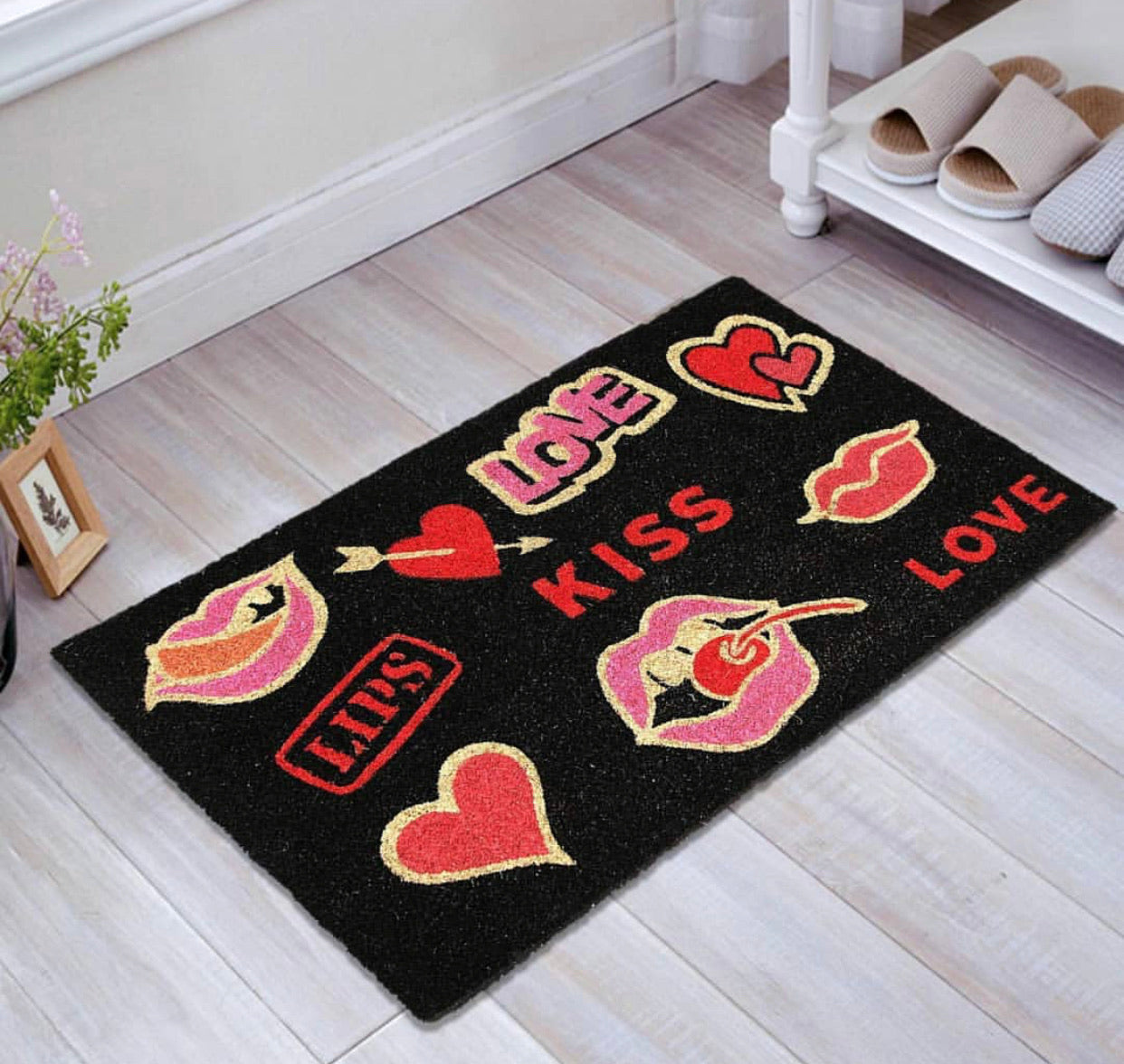 A black doormat with a colorful printed design featuring various love-themed graphics such as hearts, lips, and words related to love and affection.