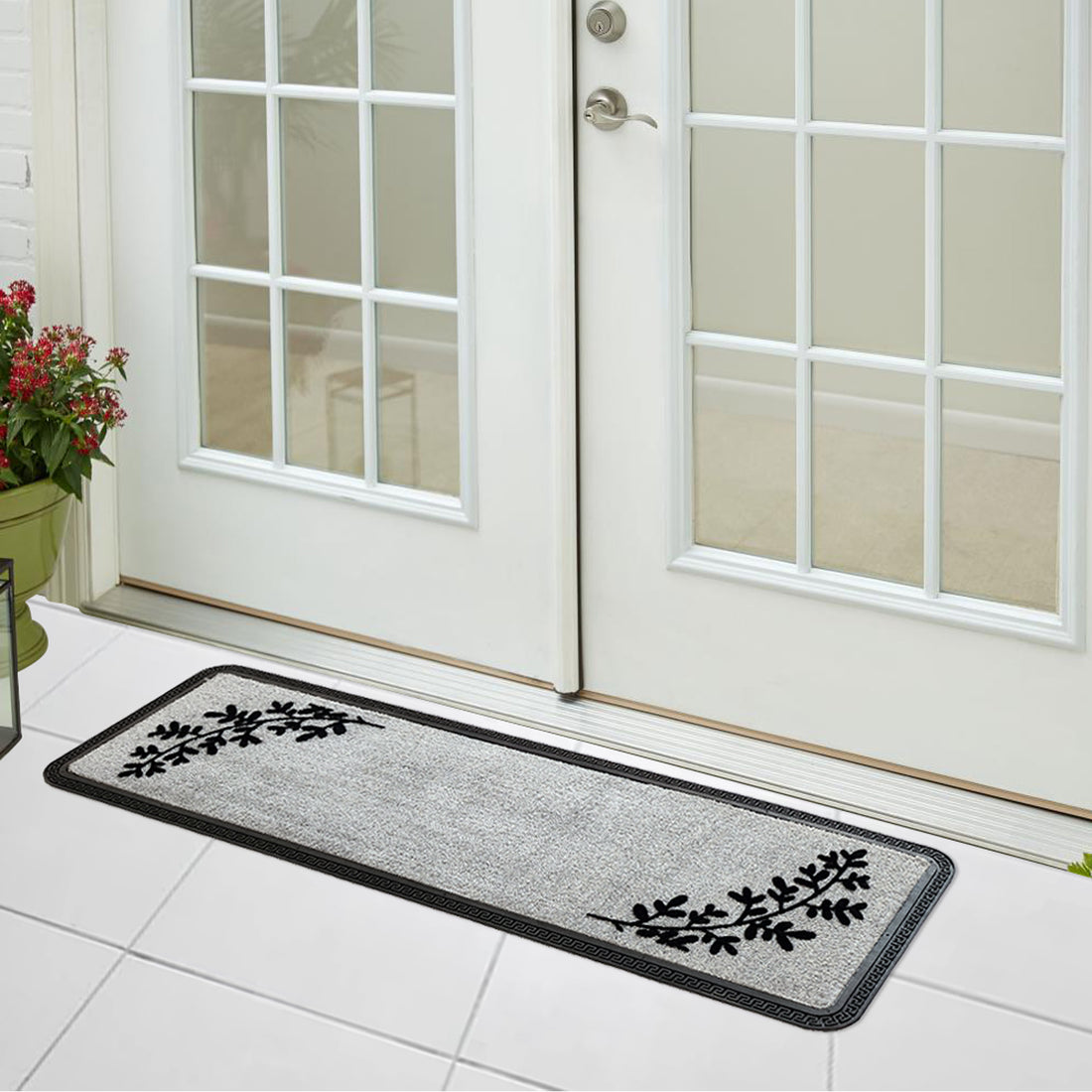 
                      
                        A grey rectangular polypropylene flocked floor mat with leaf patterns, placed on a tiled floor in front of a door.
                      
                    