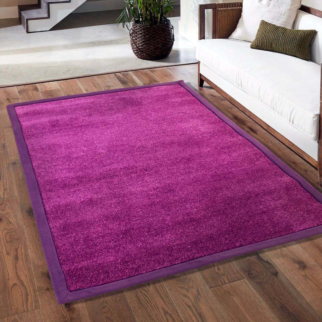 A rectangular purple luxury carpet with anti-slip backing placed on a wooden floor, with a couch and stairs in the background.