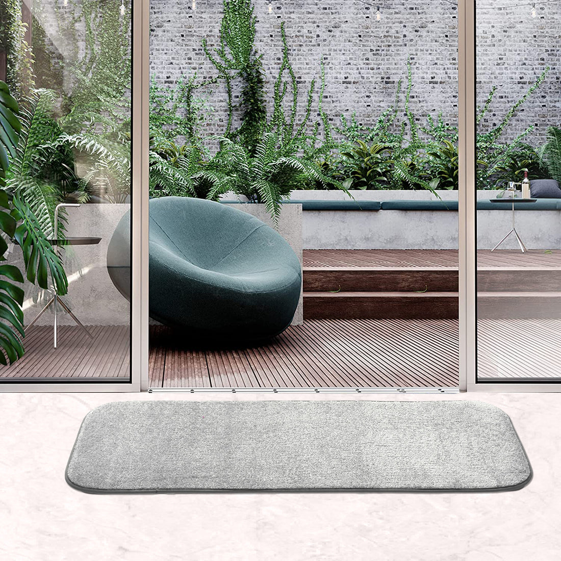 A grey anti-skid runner mat is placed on a wooden floor in front of a glass door leading to a garden, highlighting its use as an entrance mat.