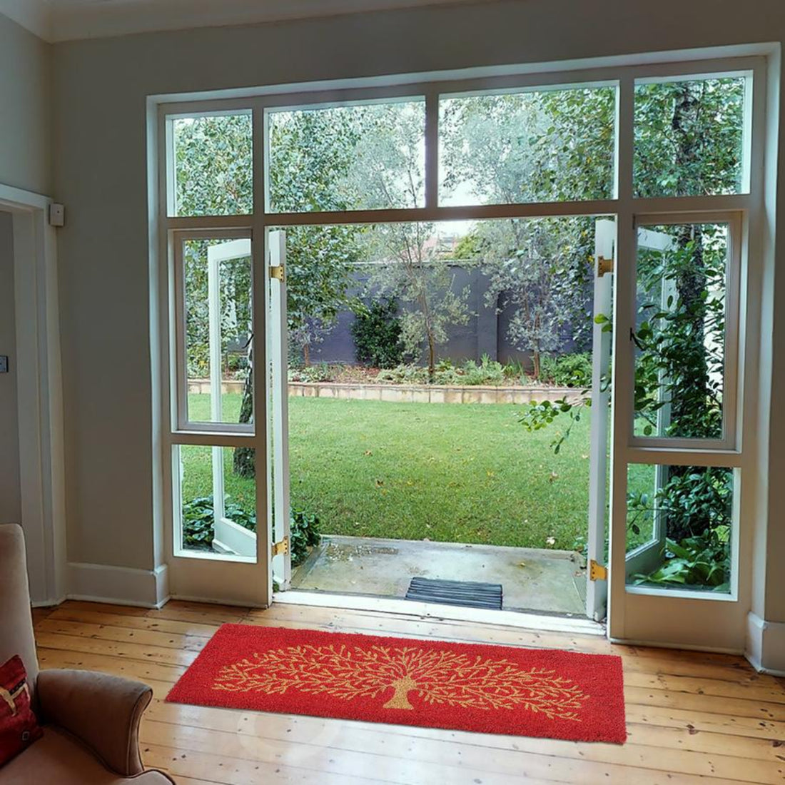 Living room with a red coir doormat featuring a tree design, leading to a glass door with a view of a garden.