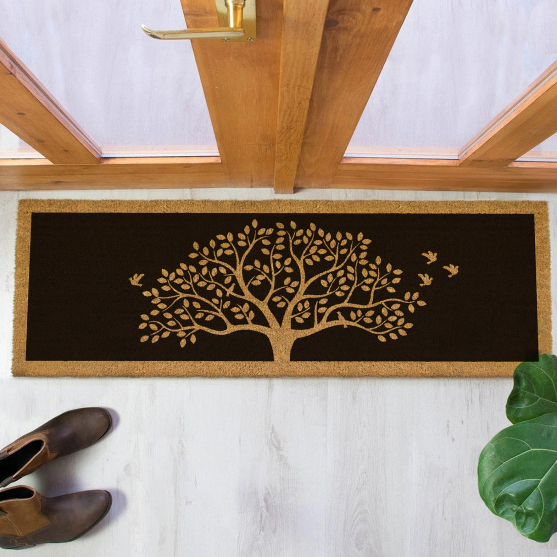 Decorative coir doormat with tree design on a white floor next to a wooden door.