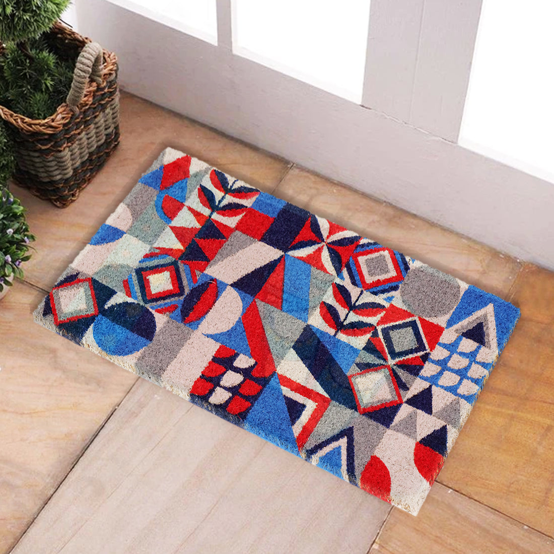 A rectangular natural coir door mat with a colorful geometric pattern featuring blue, red, and beige colors, placed on a tiled floor by a door.