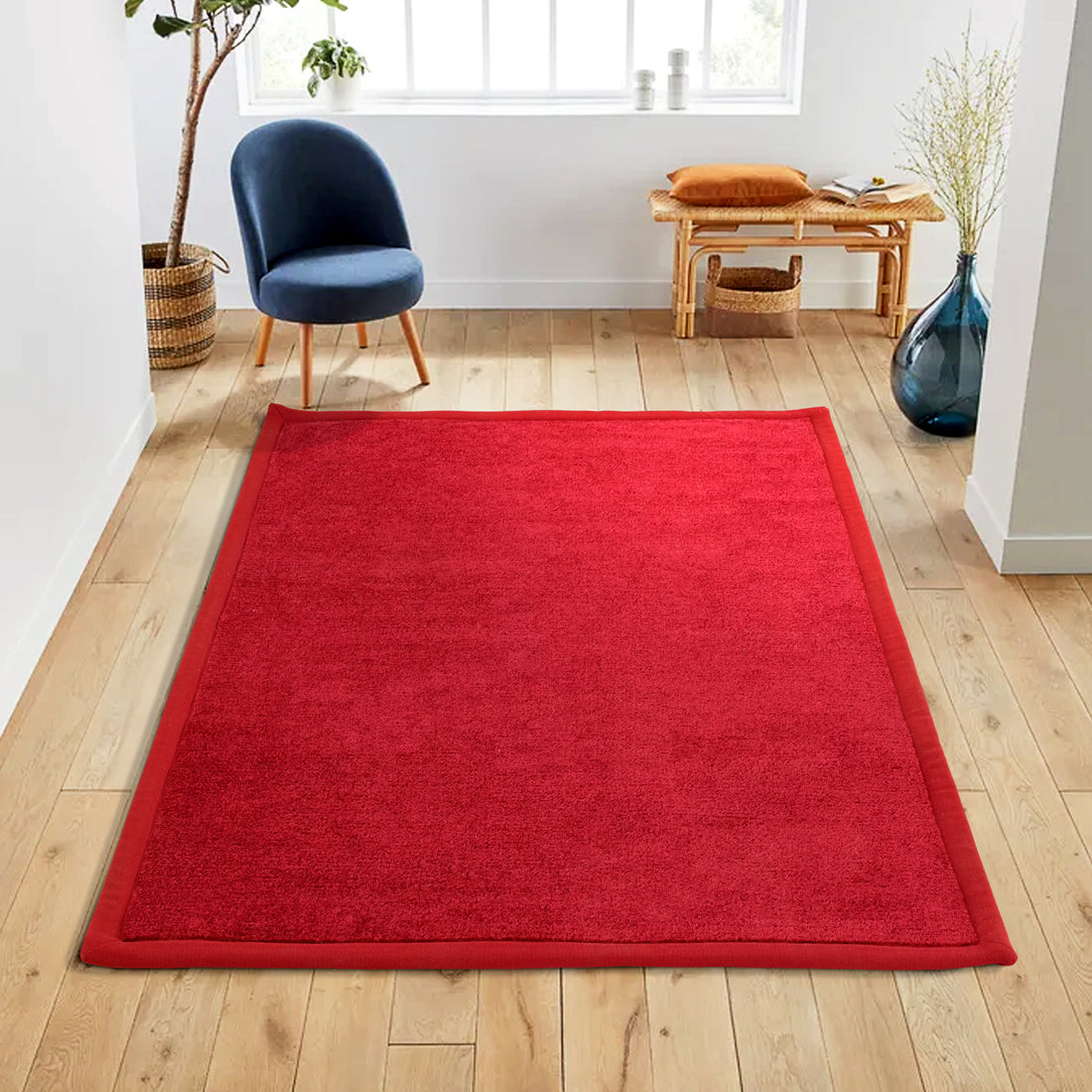 A vibrant red rectangular polypropylene carpet with anti-slip backing is placed on a wooden floor, with furniture and decorative items in the background.